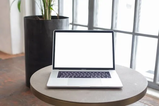 a bright small office with an empty desk ready for a new employee, a laptop and a potted plant by the window, warm daylight, editorial photography, shallow depth of field