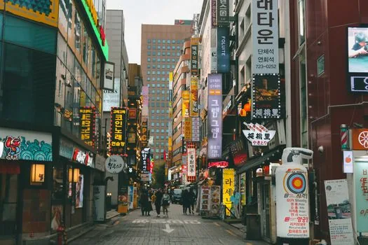 a busy new commercial district street in a Korean city at dusk, rows of small shops with warm lights, wide street view, no people in focus, editorial city photography