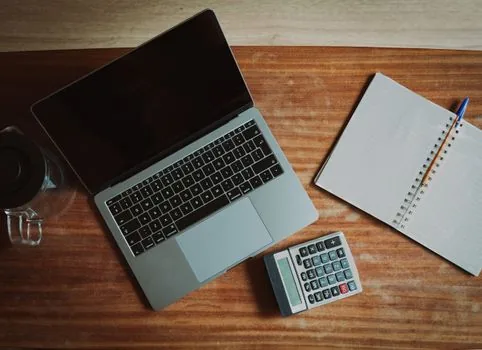 a calculator, a small notebook and a cup of coffee on a wooden shop counter, warm afternoon light through the window, korean small business interior in soft focus, editorial photography, shallow depth of field