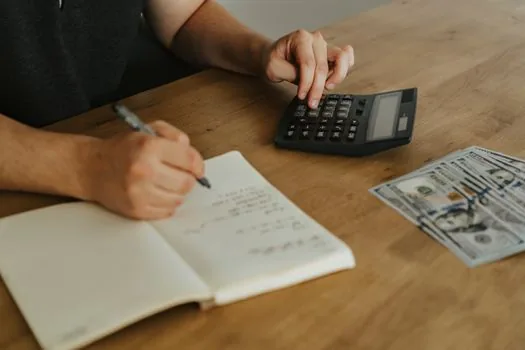 a close-up of an open accounting notebook with a calculator and several store receipts spread out on a desk, soft daylight, editorial photography