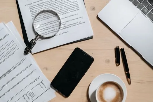a laptop on a wooden desk showing a tax office website, a smartphone and a coffee cup beside it, warm morning light through the window, editorial photography, shallow depth of field