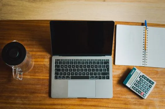 a small business owner's desk with an open laptop showing sales charts, a calculator, coffee cup and paperwork, bright tidy office, no people, editorial photography
