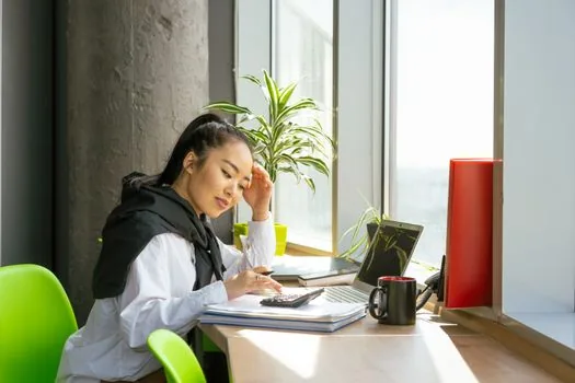 a small business owner working on paperwork and a laptop at a tidy office desk in the morning, calculator and coffee cup nearby, soft natural window light, editorial photography, shallow depth of field