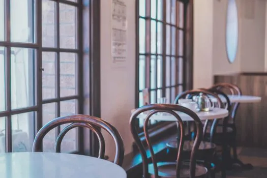 a small empty cafe interior in the daytime with chairs and a quiet counter, soft natural light coming through the window, calm and slightly somber mood, editorial photography