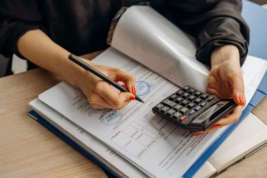 a small korean shop owner reviewing loan and bill documents with a calculator at a tidy desk, no face, soft morning window light, editorial photography, shallow depth of field