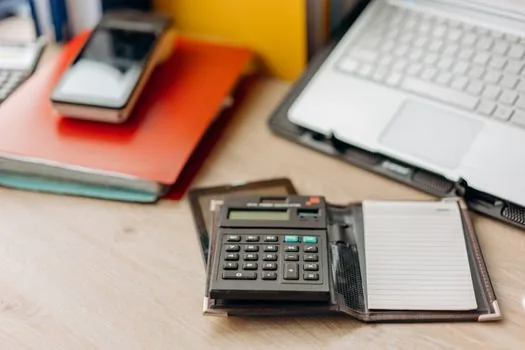 a tidy desk with a laptop showing a government tax website, a calculator and document folders, no people, soft window light, editorial photography, shallow depth of field