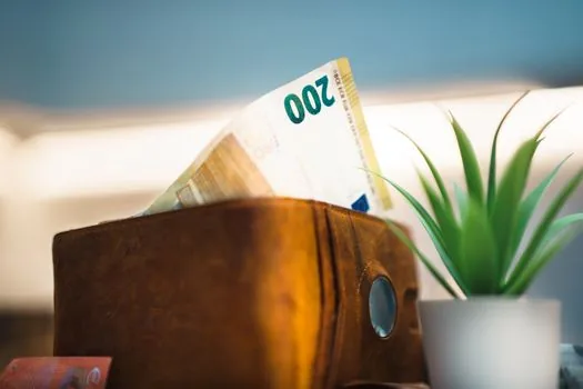 a yellow umbrella standing beside a piggy bank and a small notebook on a calm wooden table, soft natural light, financial saving concept, editorial still life photography