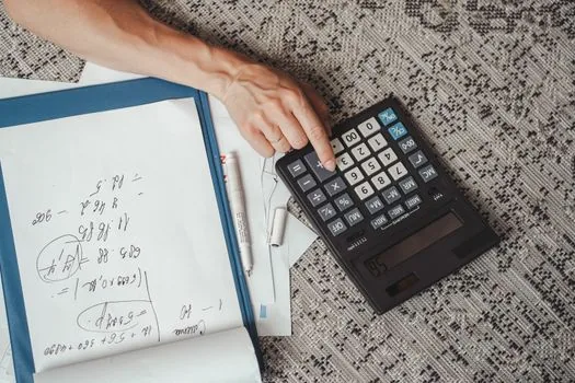 an open simple accounting notebook with handwritten numbers and a pen beside a small calculator on a desk, warm afternoon light, editorial photography, shallow depth of field
