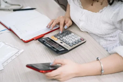 a Korean small business owner comparing loan documents at a wooden cafe counter, calculator and notebook, soft daylight, over-the-shoulder view, editorial photography