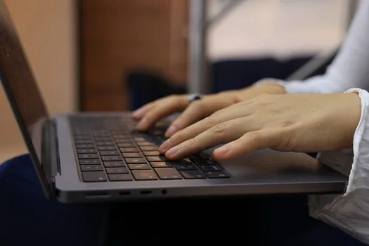 a person filling out an online government support application on a laptop at a small business office, hands on keyboard, close-up, soft daylight, editorial photography