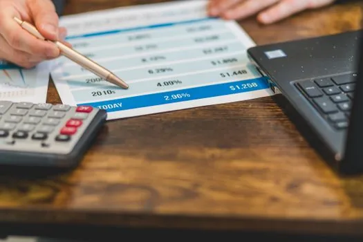 a small shop owner reviewing loan and guarantee documents at a wooden counter, laptop and calculator beside, soft window light, editorial photography, shallow depth of field