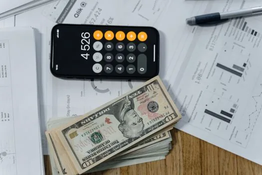 a stack of business documents and a calculator on a wooden desk at a small korean shop counter, warm afternoon light, close-up, editorial photography, shallow depth of field