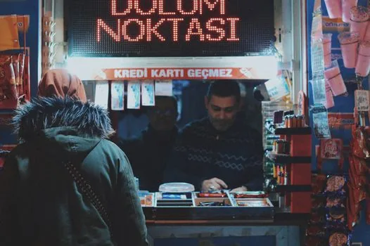 a worried small business owner reviewing unpaid loan documents at a small shop counter, warm evening light, over-the-shoulder view, editorial photography