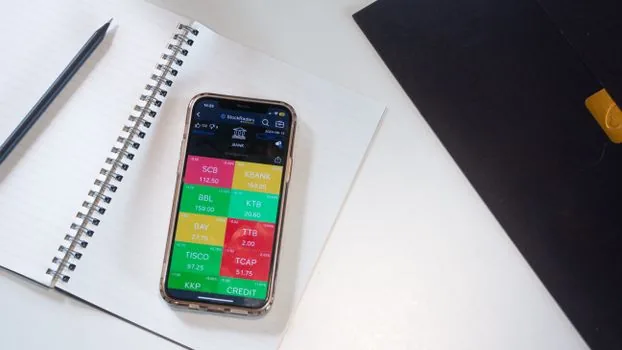 a young person reviewing a savings account on a smartphone banking app at a small home desk, coins and a notebook nearby, soft window light, editorial photography, no text