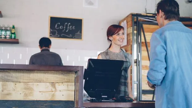 a young small business owner reviewing paperwork and a calculator at a cozy cafe counter, warm afternoon light, over-the-shoulder view, no face closeup, editorial photography