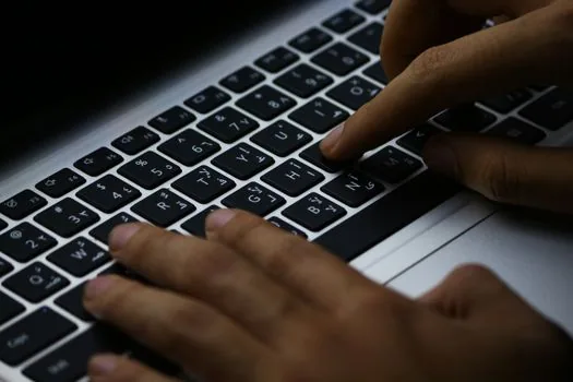 person filling out an online government application on a laptop at a small business counter, focused hands on keyboard, soft indoor light, editorial photography, no text