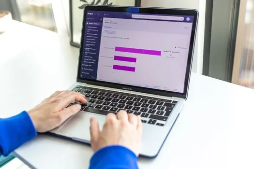 shop owner hands checking an official support program listing on an unbranded laptop at a bright small shop counter, blank interface cards, soft daylight, clean editorial photography, no face, no logo, no readable text