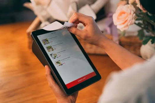Korean restaurant counter with origin labeling board, printed menu, ingredient delivery invoices, and tablet showing delivery app menu edit screen