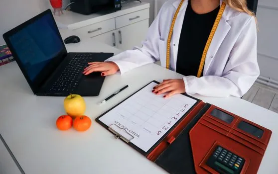 Korean small business owner posting a hiring notice on laptop, printed staff schedule and calendar on desk, bright office documentary photo