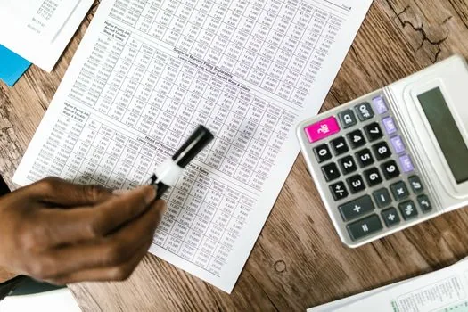 Korean small restaurant owner reviewing monthly sales spreadsheet, food cost invoices, payroll sheet, and rent memo on a stainless kitchen table