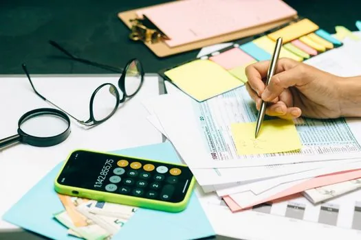 Korean sole proprietor comparing first half sales report, expense receipts and tax prepayment estimate sheet, realistic office photo | 상반기 매출과 비용 자료로 추계신고 여부를 검토하는 장면
