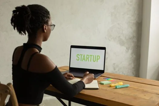 Korean startup founder downloading official business plan attachment from government startup notice, laptop and printed checklist on desk
