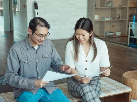 Korean tax advisor and small business owner reviewing phased schedule checklist and property documents in office meeting