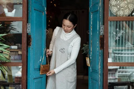 Korean cafe owner attaching CCTV privacy notice near store entrance, security camera visible above door, clean retail interior, no readable private data | 매장 출입구에서 CCTV 안내판 문구와 위치를 확인하는 모습