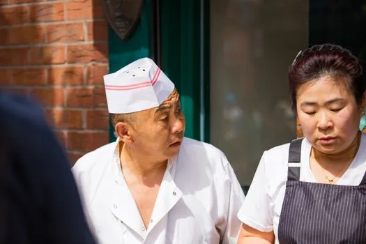 Korean restaurant owner comparing food business license copy with government application checklist and laptop, realistic daylight photo