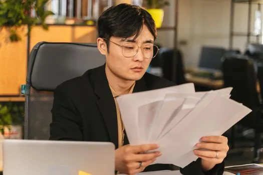 Korean small business owner arranging employment contract payroll memo and business registration certificate on desk | 첫 직원 채용 후 4대보험 신고 전 서류를 정리하는 장면