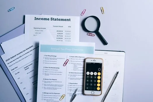 Korean small business owner reviewing deduction application papers with calculator and income records on office desk