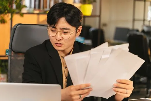 Office manager checking delegation letter, corporate seal certificate and employee ID before bank visit, Korean corporate paperwork scene | 대리 방문 전 위임장과 법인인감증명서를 확인하는 장면