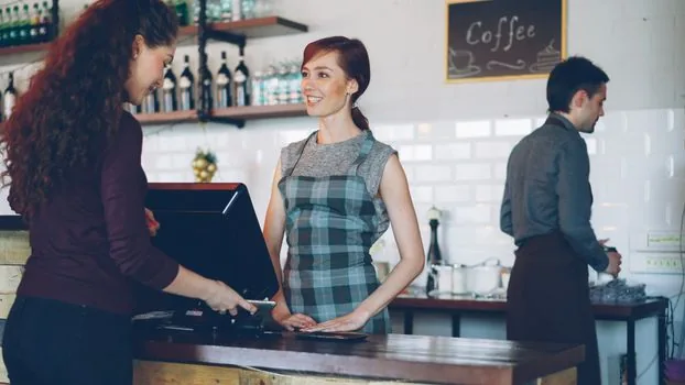 Small cafe counter with QR payment stand, owner phone merchant app and opening checklist calendar | QR코드 배송 뒤 매장 카운터에 설치하고 가맹점앱을 확인하는 장면